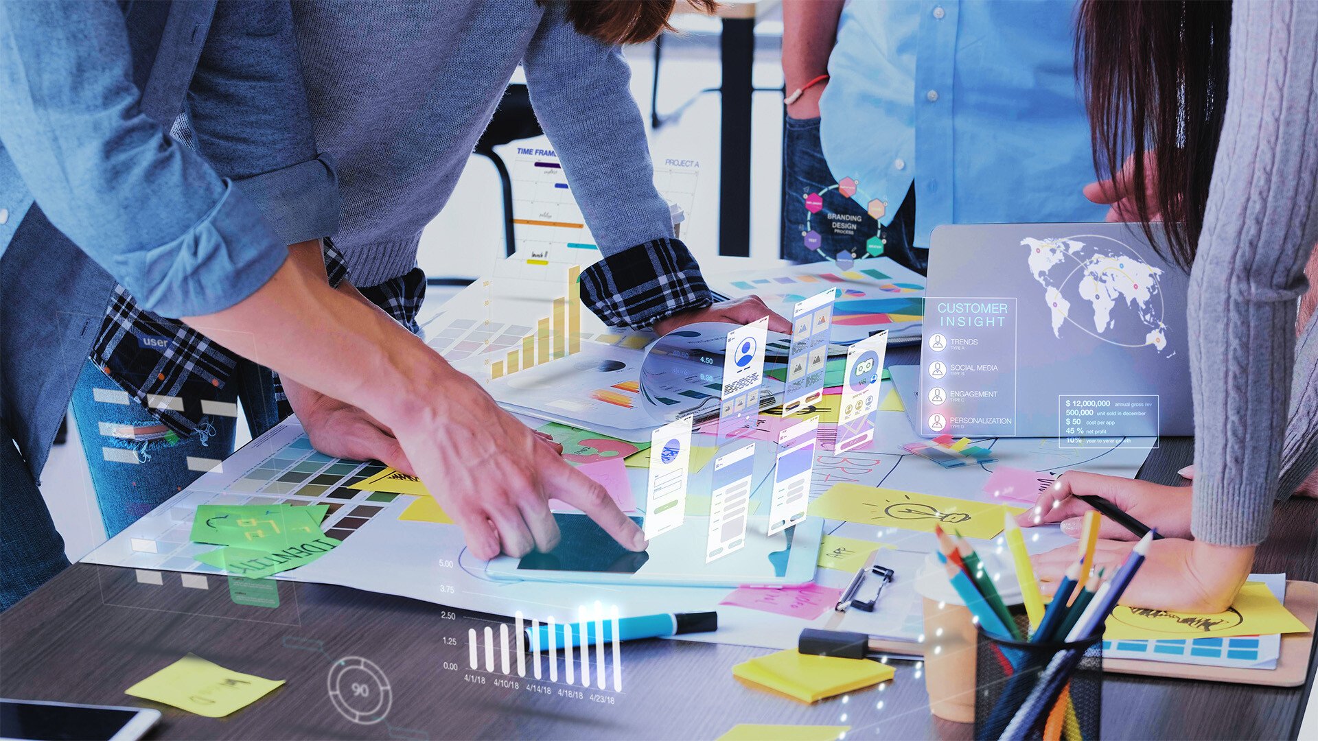 Holographic images rise up from a desk as a person points to an image.
