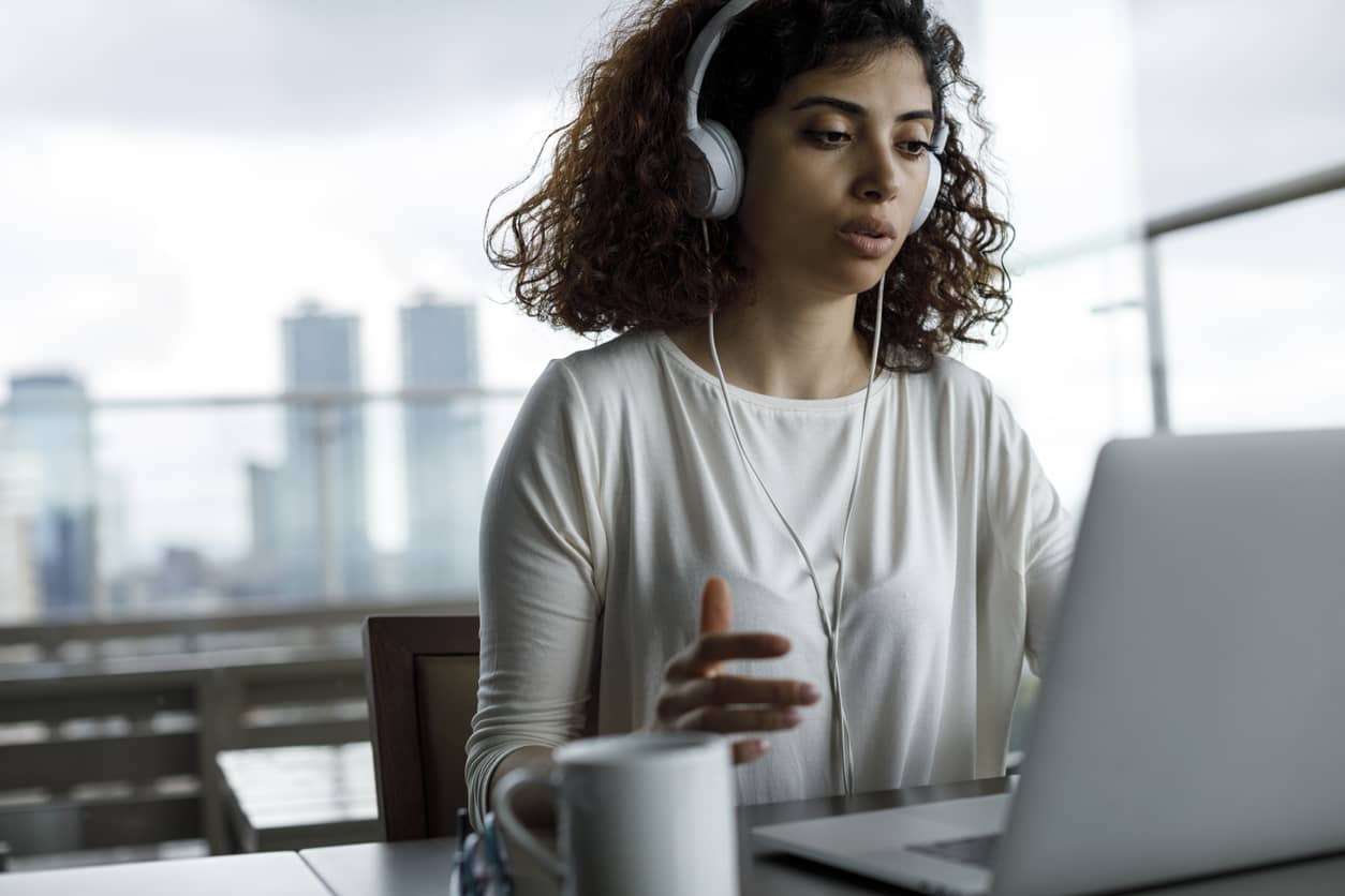 corporate remote learning, with an adult learner engaging in a conversation on her laptop with noise-cancelling headphones and a coffee